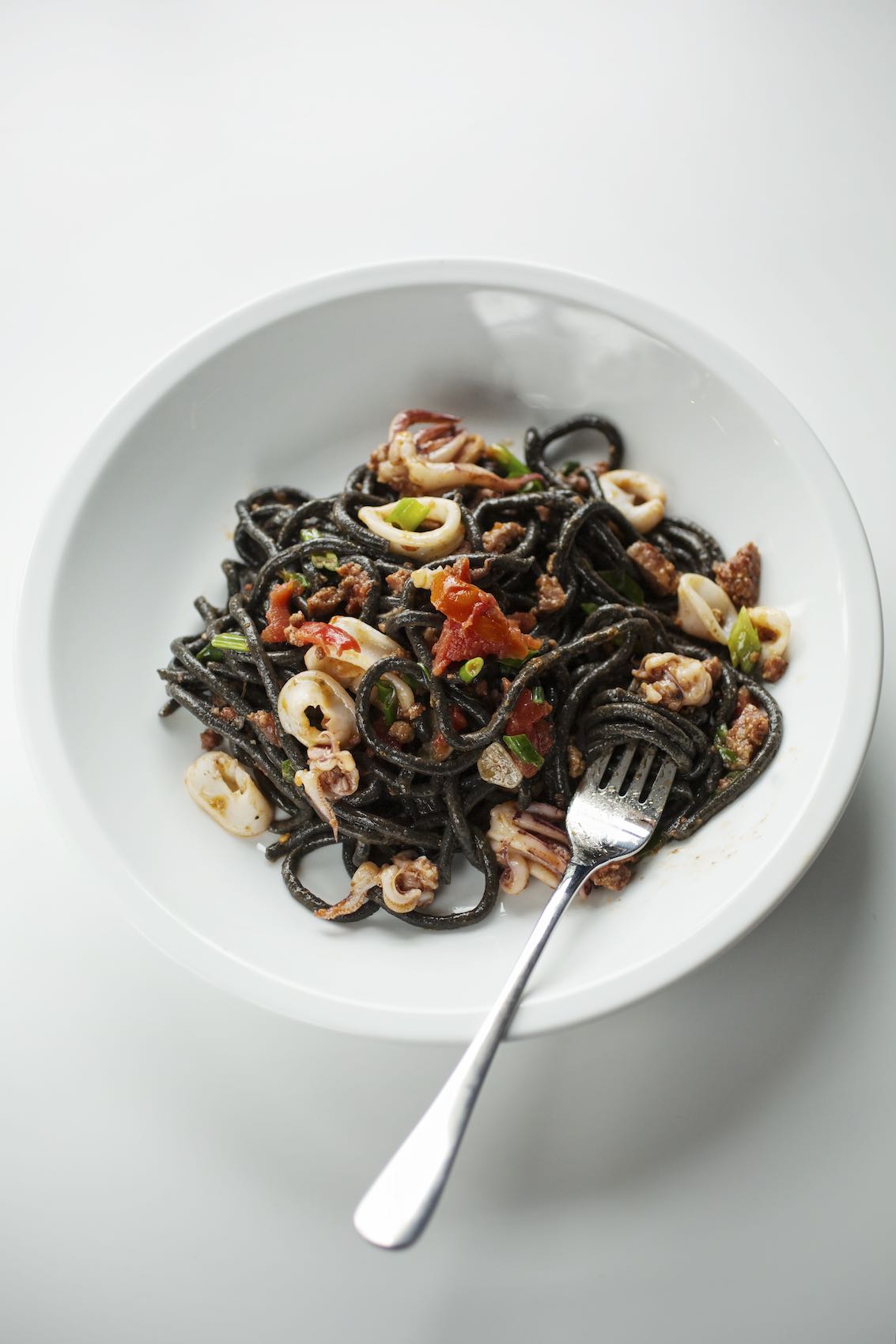 Jody Horton Photography - Squid ink spaghetti with calamari in a white bowl.