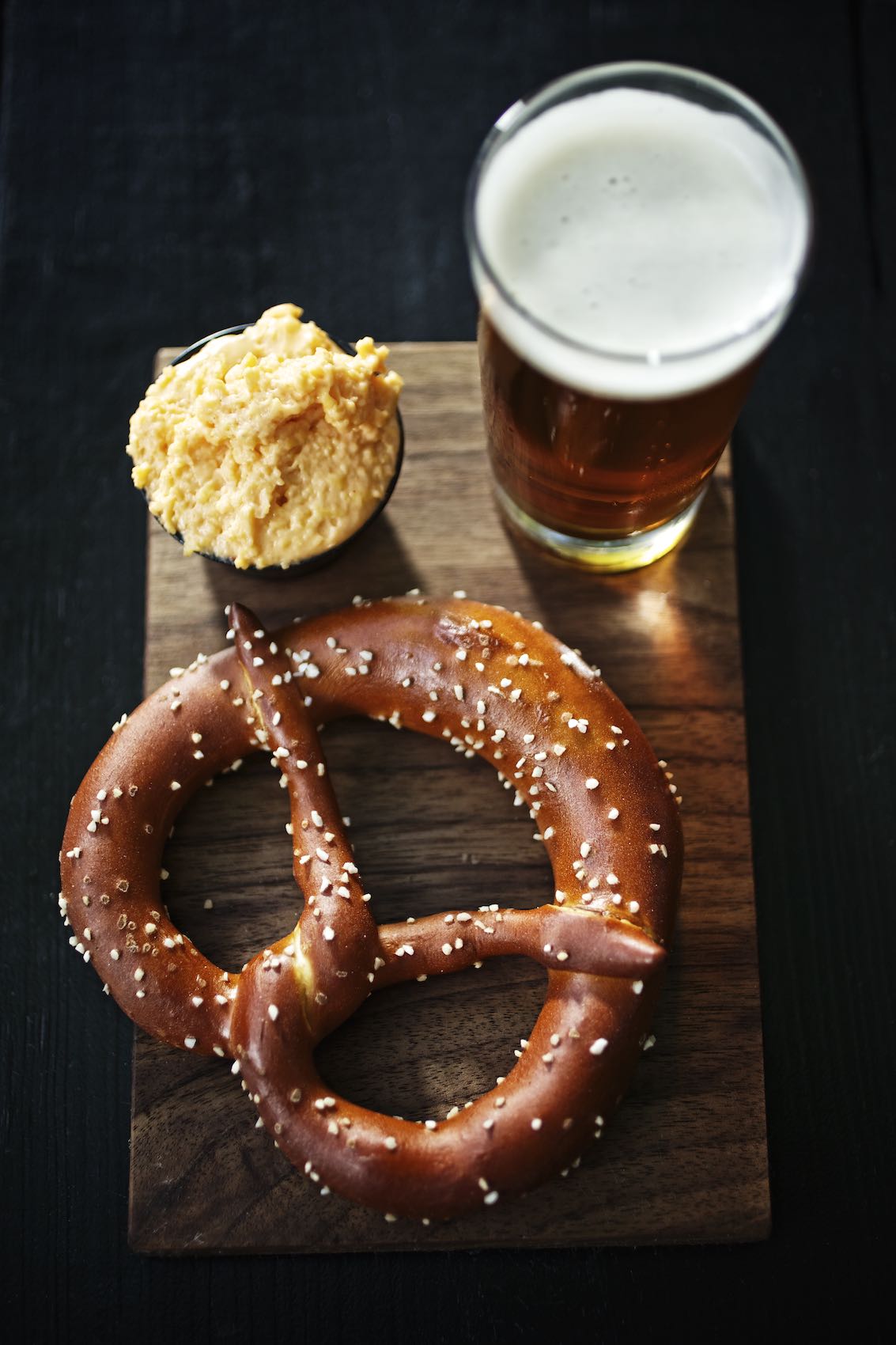 Jody Horton Photography - Baked pretzel, cheese sauce, and draft beer on a wooden board. 