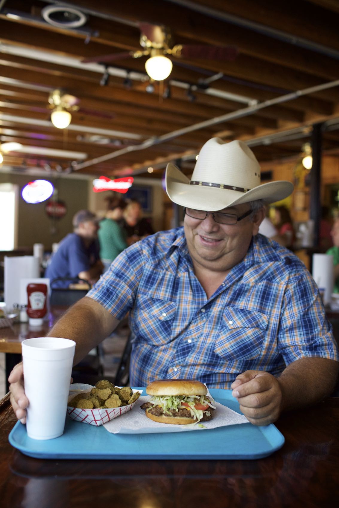 Jody Horton Photography - Man in cowboy hat eating a burger in roadhouse-like restaurant. 