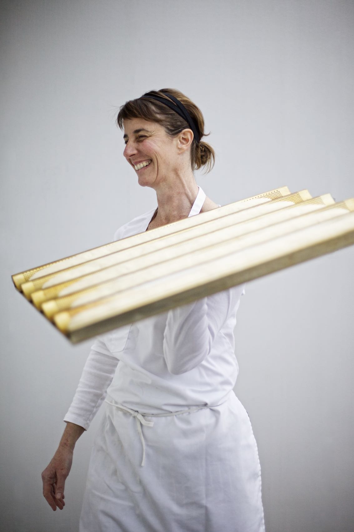Jody Horton Photography - Woman baker in uniform, smiling while carrying unbaked baguettes. 