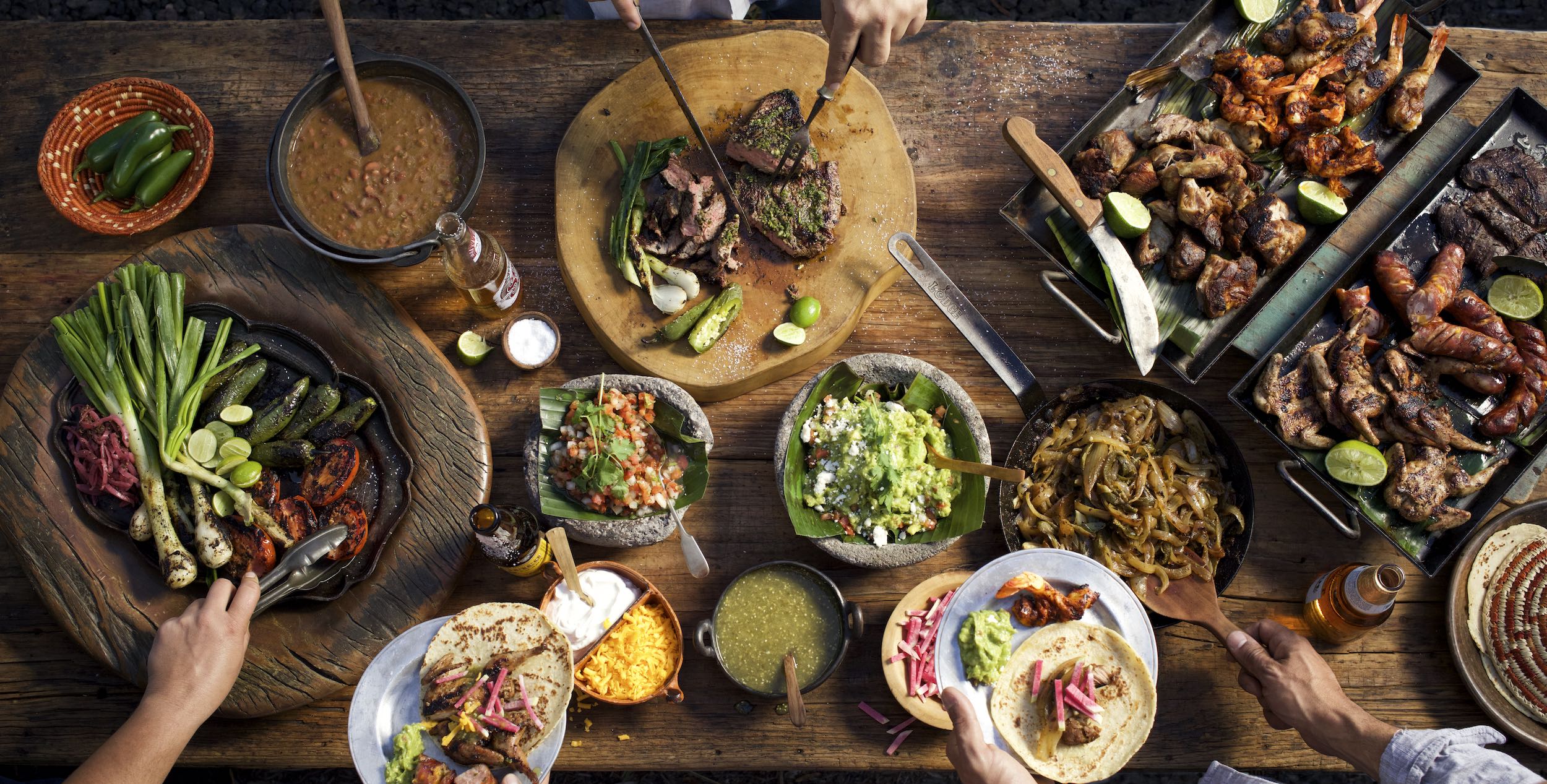 Jody Horton Photography - Taco spread on a wooden table with hands reaching and plating food.