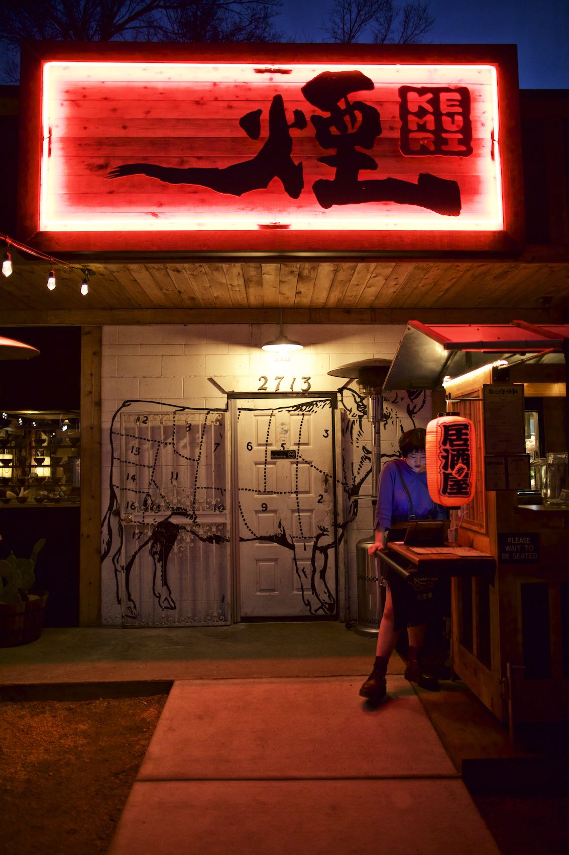 Jody Horton Photography - Hostess standing under the neon sign of Kemuri restaurant. 