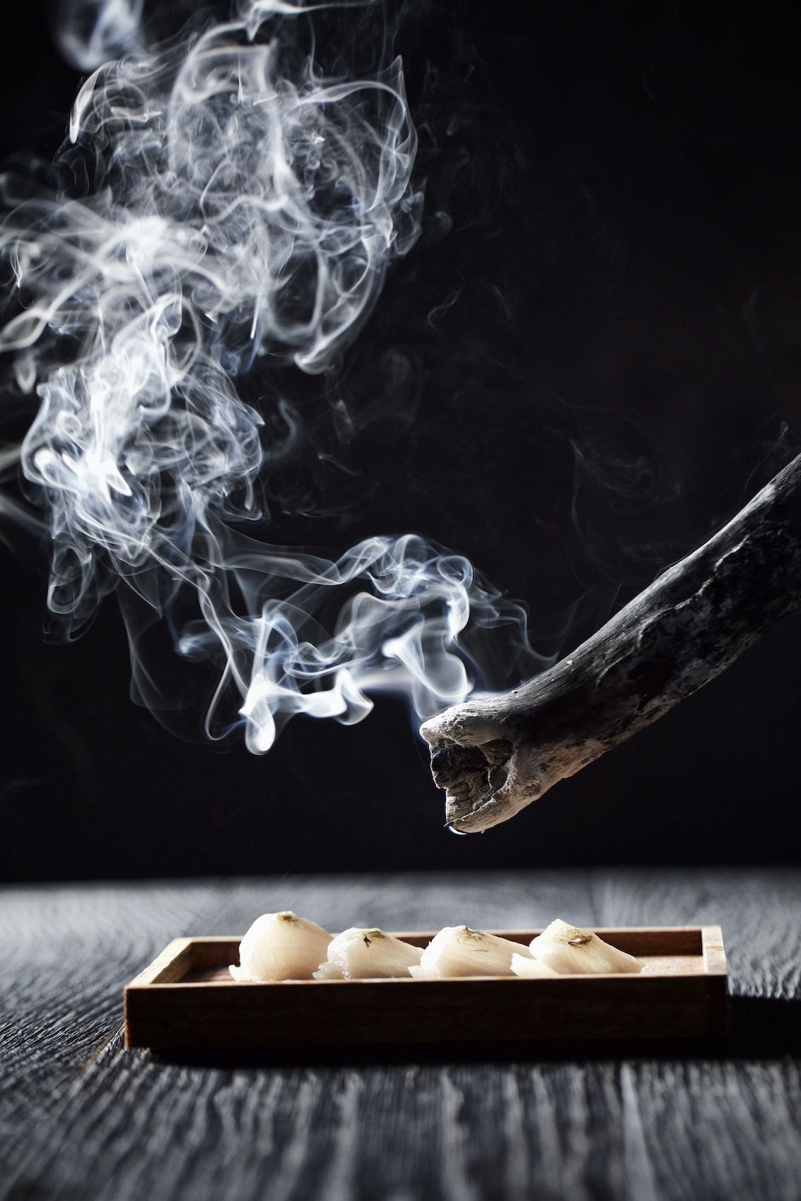 Jody Horton Photography - Charred wood being used to smoke sashimi on a black table. 