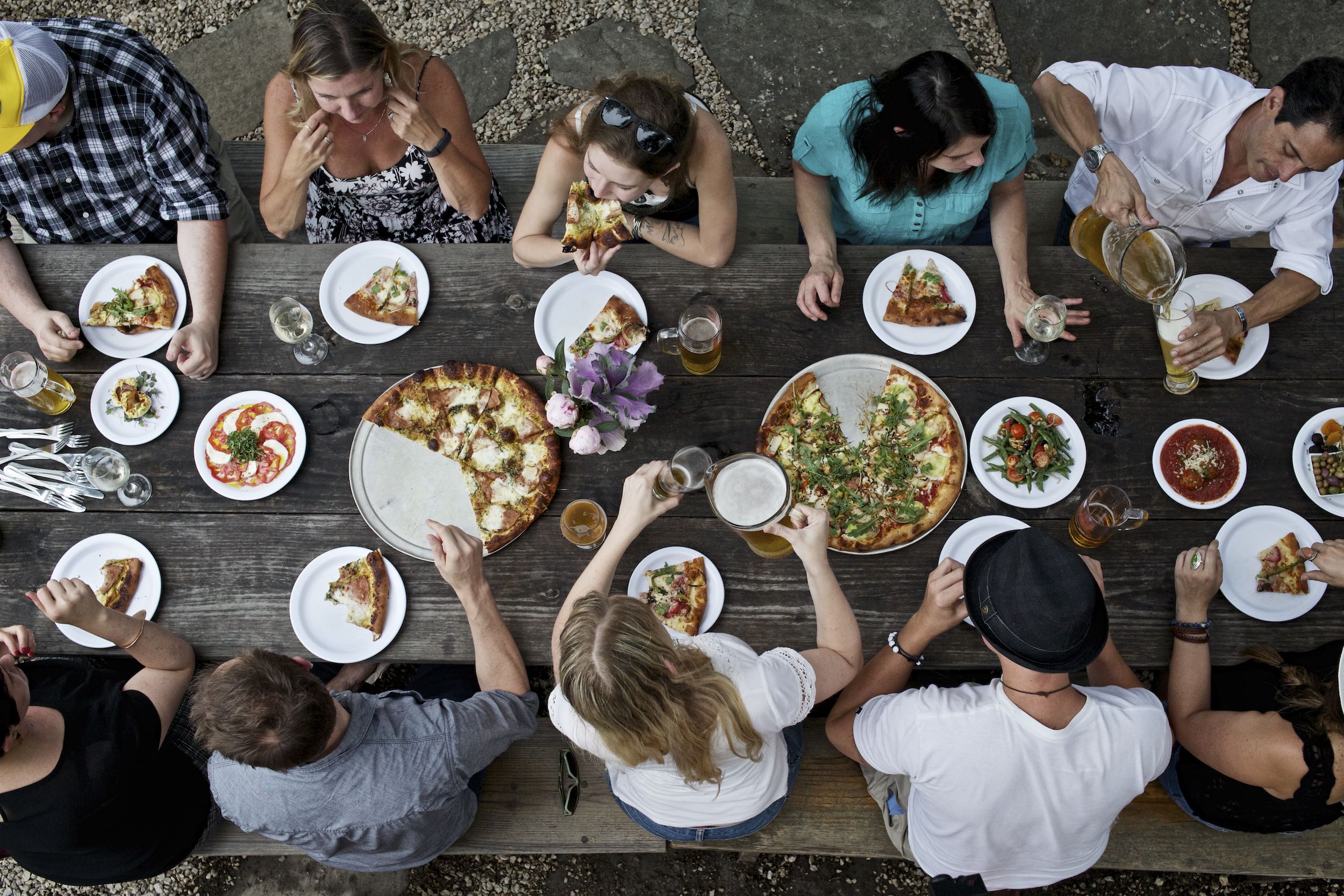 Jody Horton Photography - Friends gather around wood picnic table to eat pizza and drink beer. 