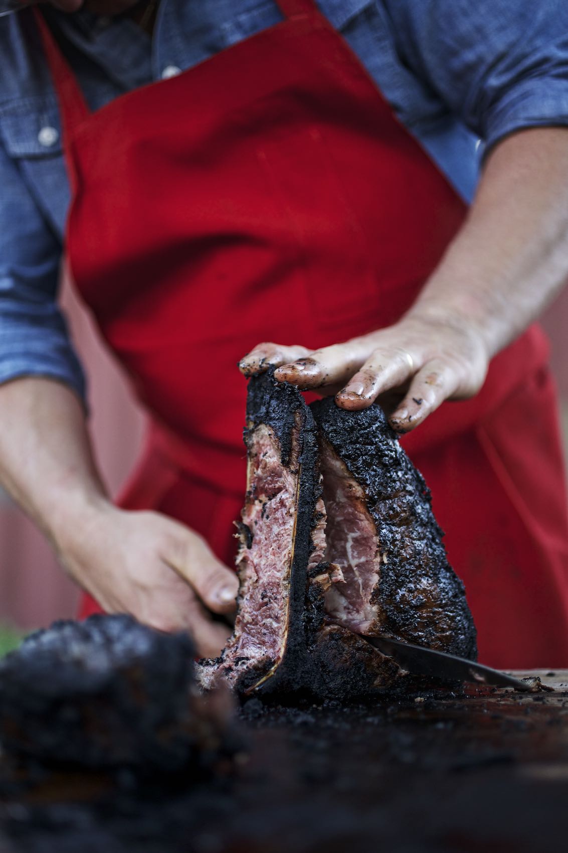 Jody Horton Photography - Chef carves barbecued meat on outdoor table.