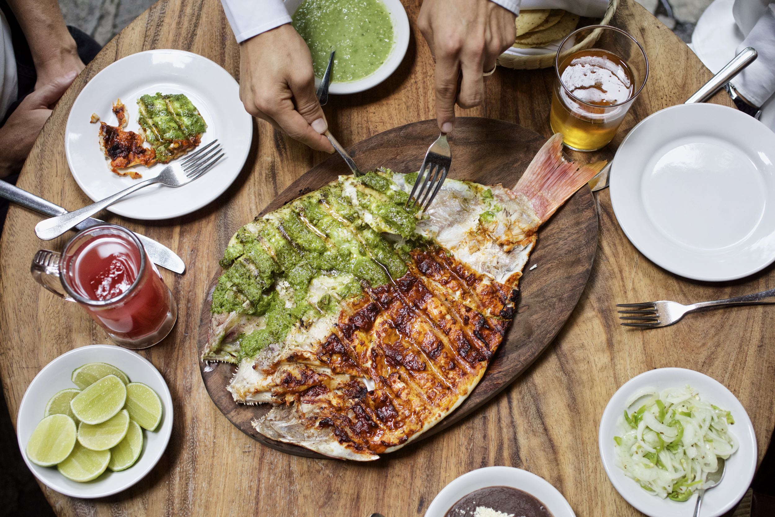 Jody Horton Photography - Mexico City dinner spread with cooked fish and beverages on a wood table. 