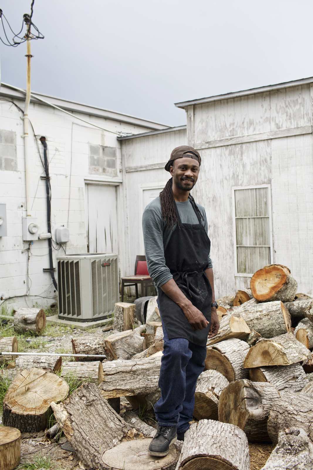 Jody Horton Photography - Cook standing among piles of chopped wood.