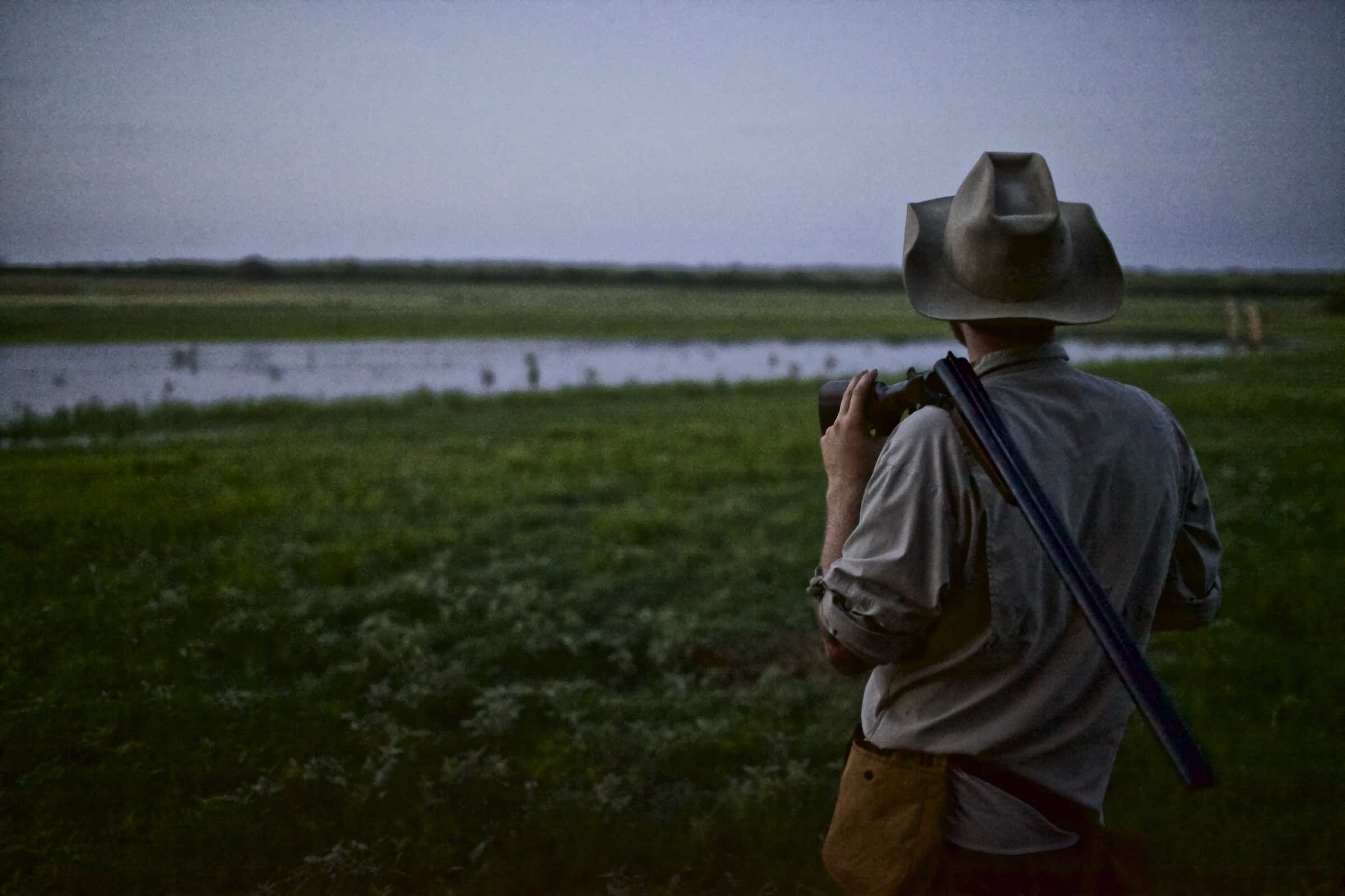 Jody Horton Photography - Hunter facing an open field with his rifle over his shoulder.