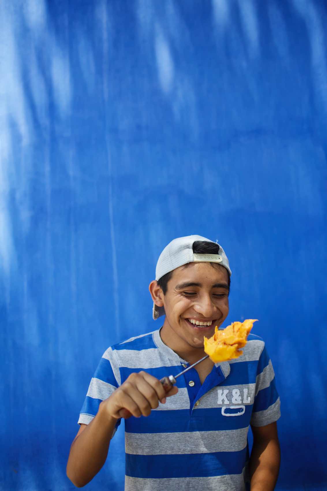 Jody Horton Photography - Young man eating mango off a skewer. 