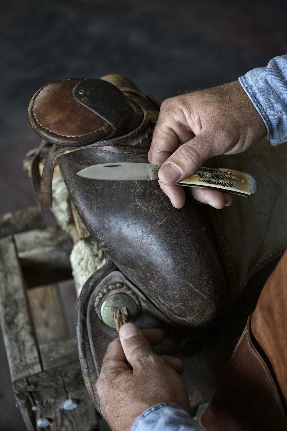Hands using a knife to work on a western saddle. 