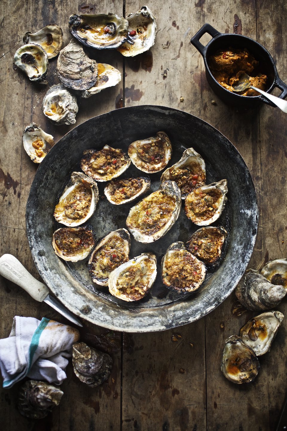 Grilled, half-shell oysters presented in a rustic, metal bowl.