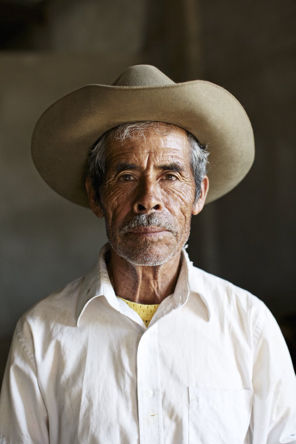 Portrait of mezcal farmer in a white button down and brown hat. 