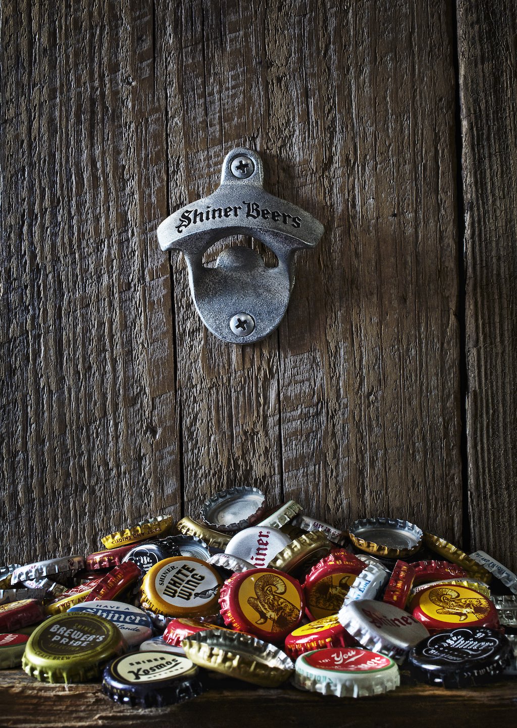 Bottle opener and various beer caps against a wood wall. 