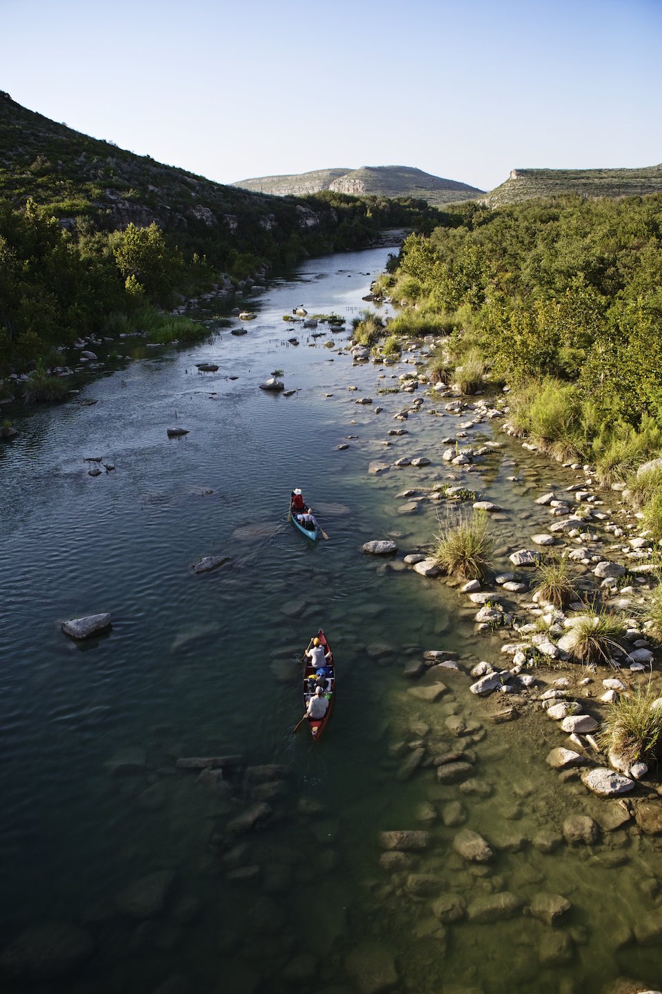 Two canoes traveling down a shallow and rocky riverbed.