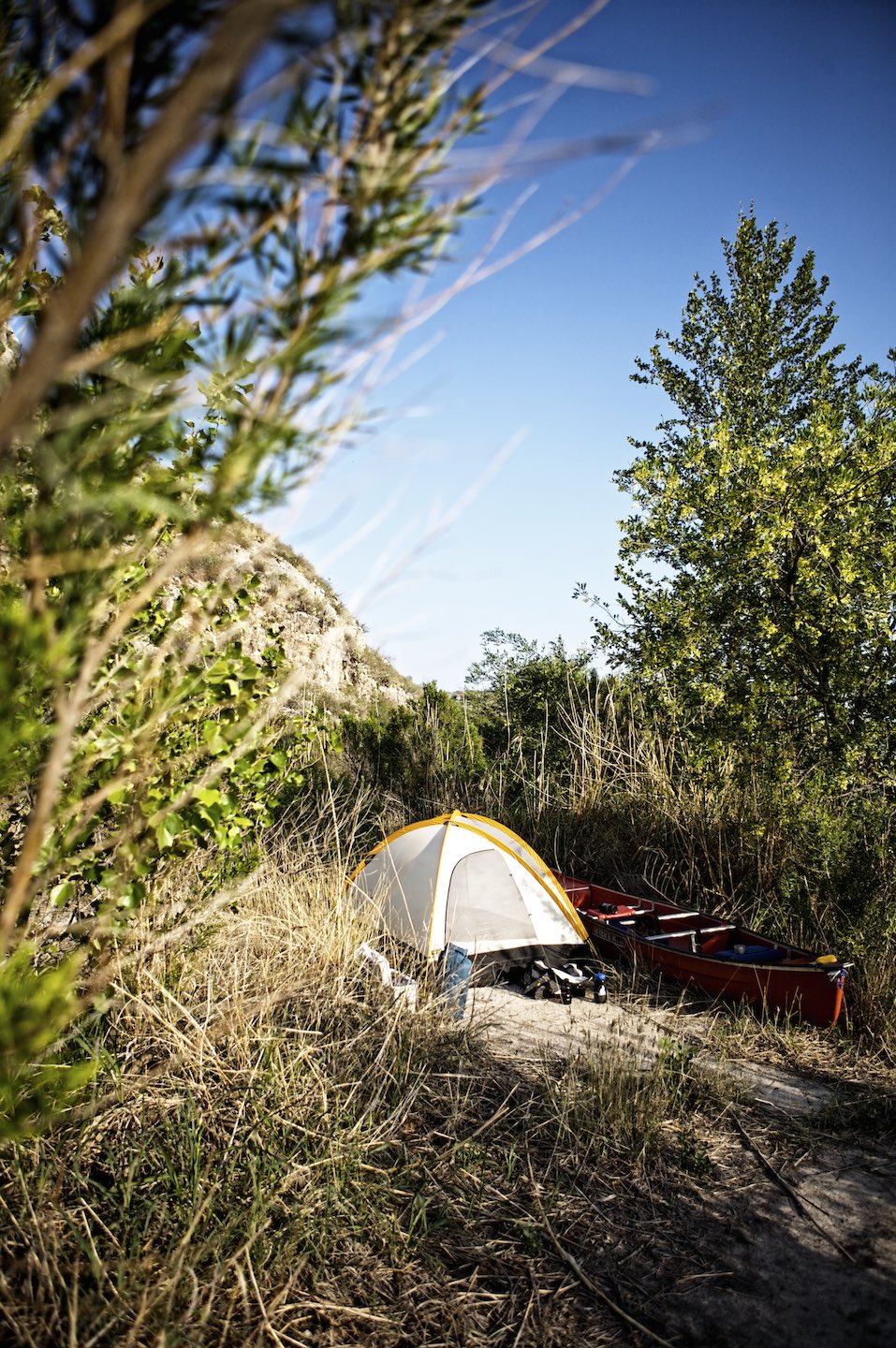 A lone tent and a canoe surrounded by greenery in the wilderness. 