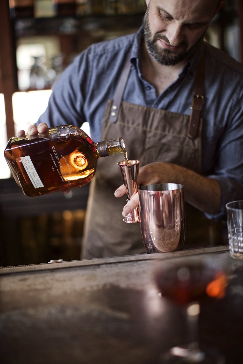 Bartender making a cocktail using Woodford Reserve whiskey and brass tools. 