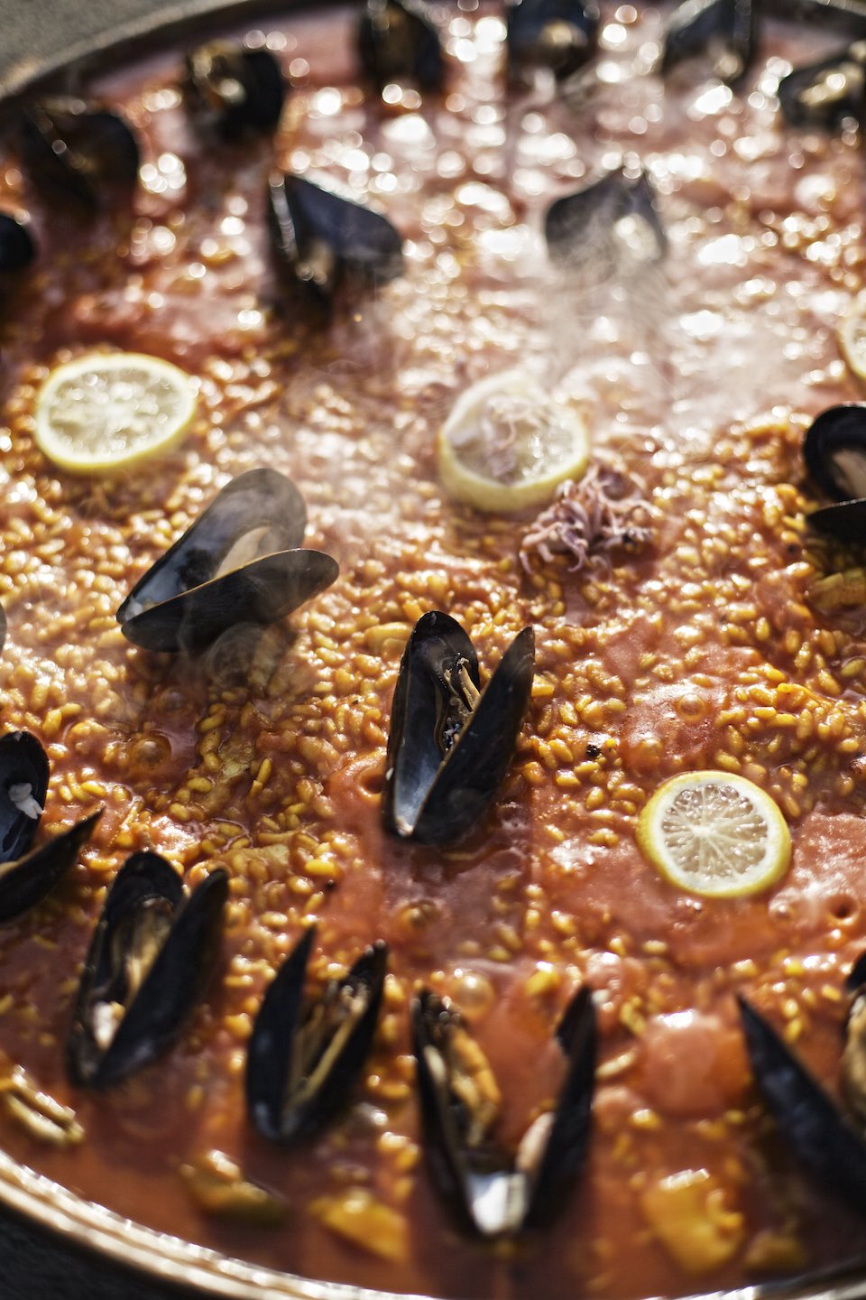 A steaming pan of seafood paella with mussels and lemon. 