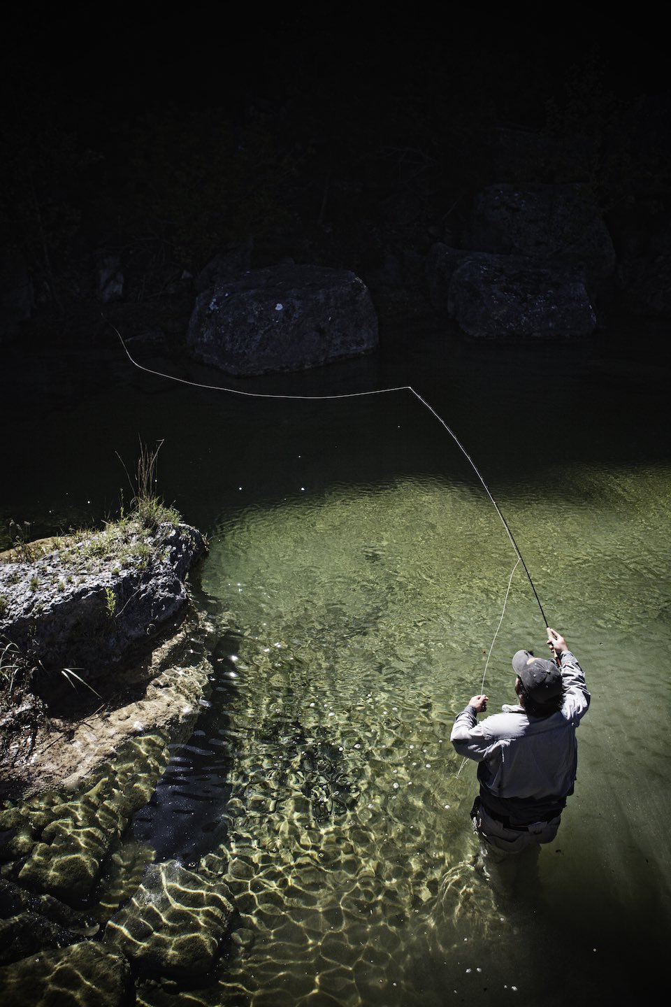 Fisherman casting a line while standing in shallow water. 