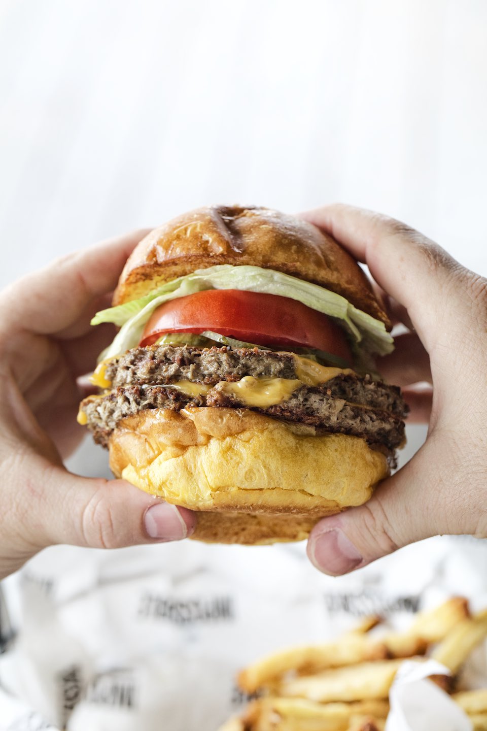 Hands holding a classic, double cheeseburger on a brioche bun. 