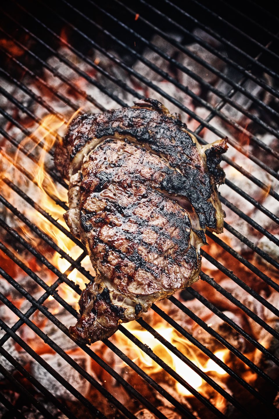 Ribeye steak cooking on a charcoal grill. 