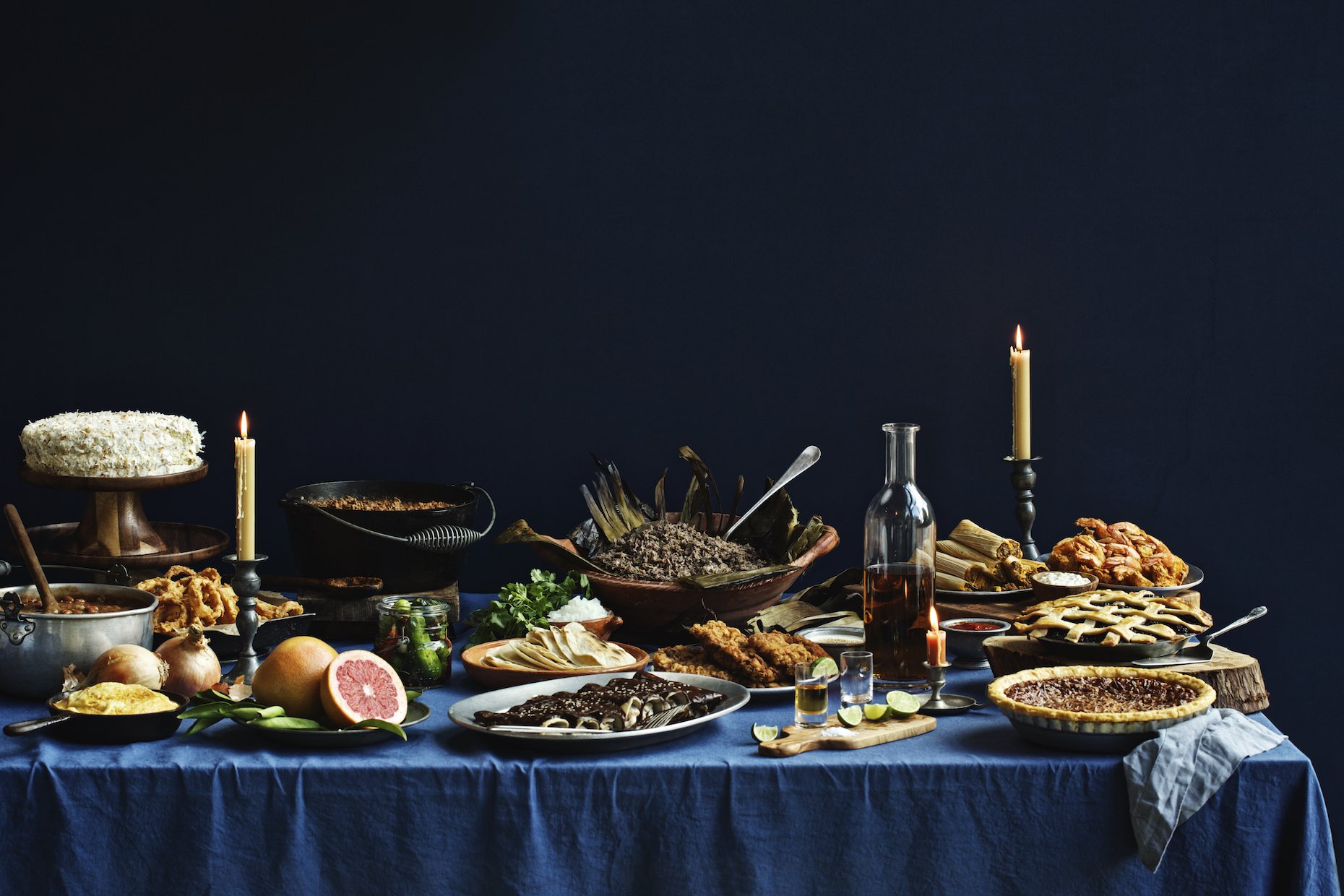 Candlelit dinner spread set on a blue table cloth in a dark blue room. 