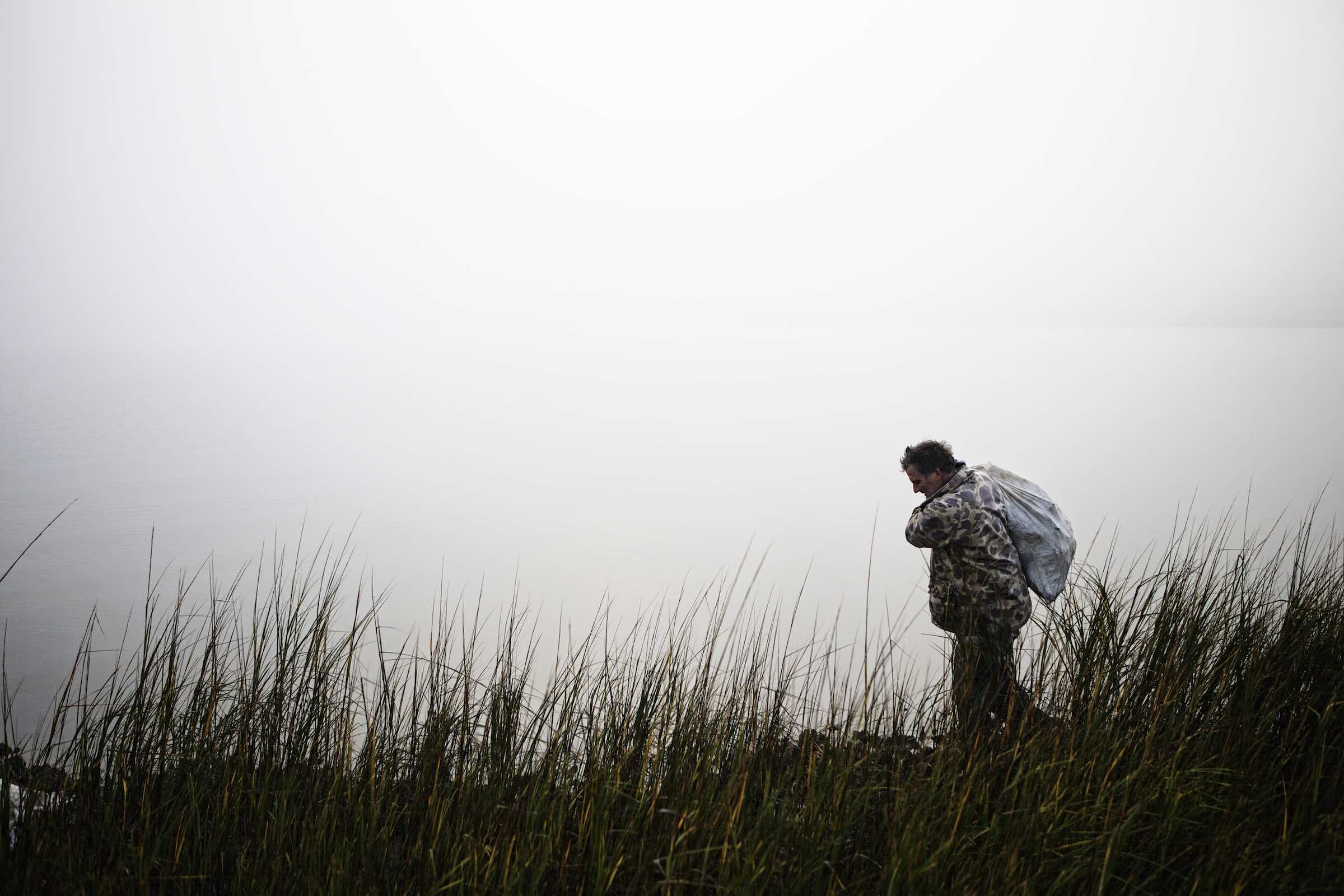 Jody Horton Photography - Fisherman hauling a heavy sack through tall grass. 