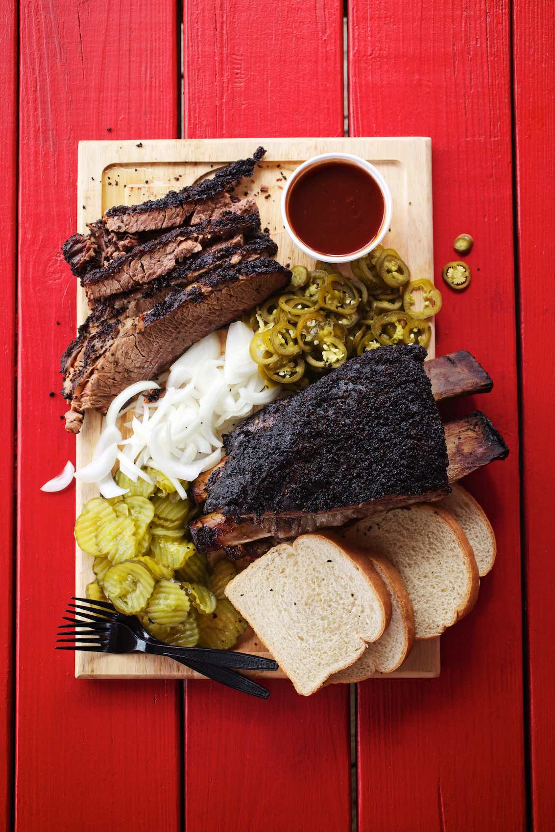 Jody Horton Photography - Barbecue spread on cutting board on red picnic table. 