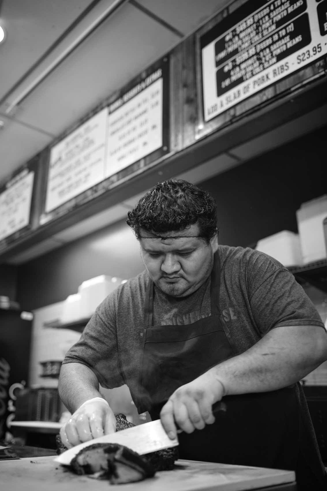 Jody Horton Photography - Cook slicing meat on kitchen line, shot in B&W.