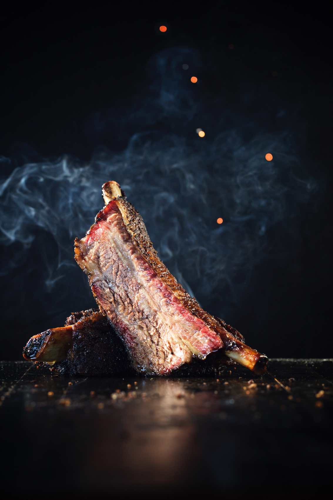 Jody Horton Photography - Steaming barbecue ribs on black table.