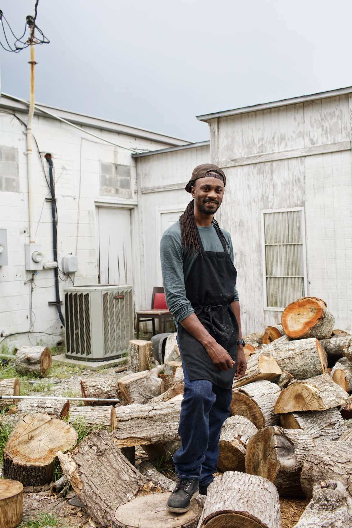 Jody Horton Photography - Chef stands outside among chopped wood.