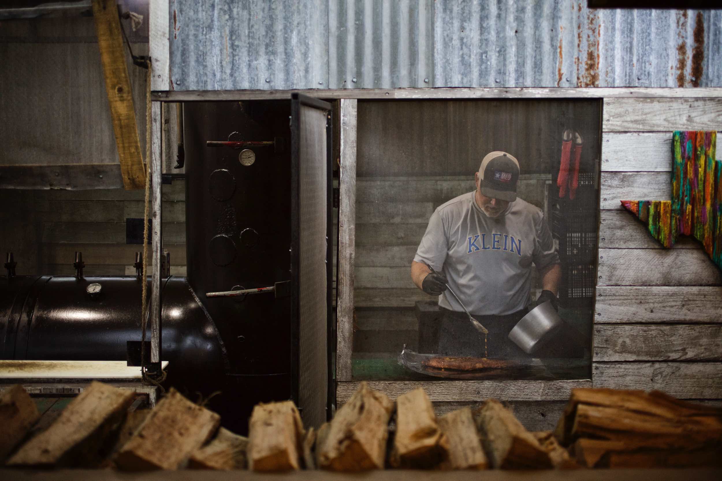 Jody Horton Photography - Man preparing meat behind mesh window of rustic building. 