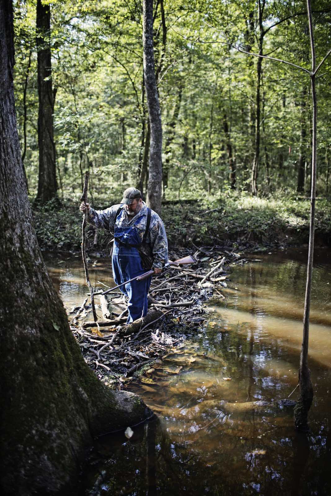 Jody Horton Photography - Hunter carrying a shot gun while crossing a stick bridge across the water. 