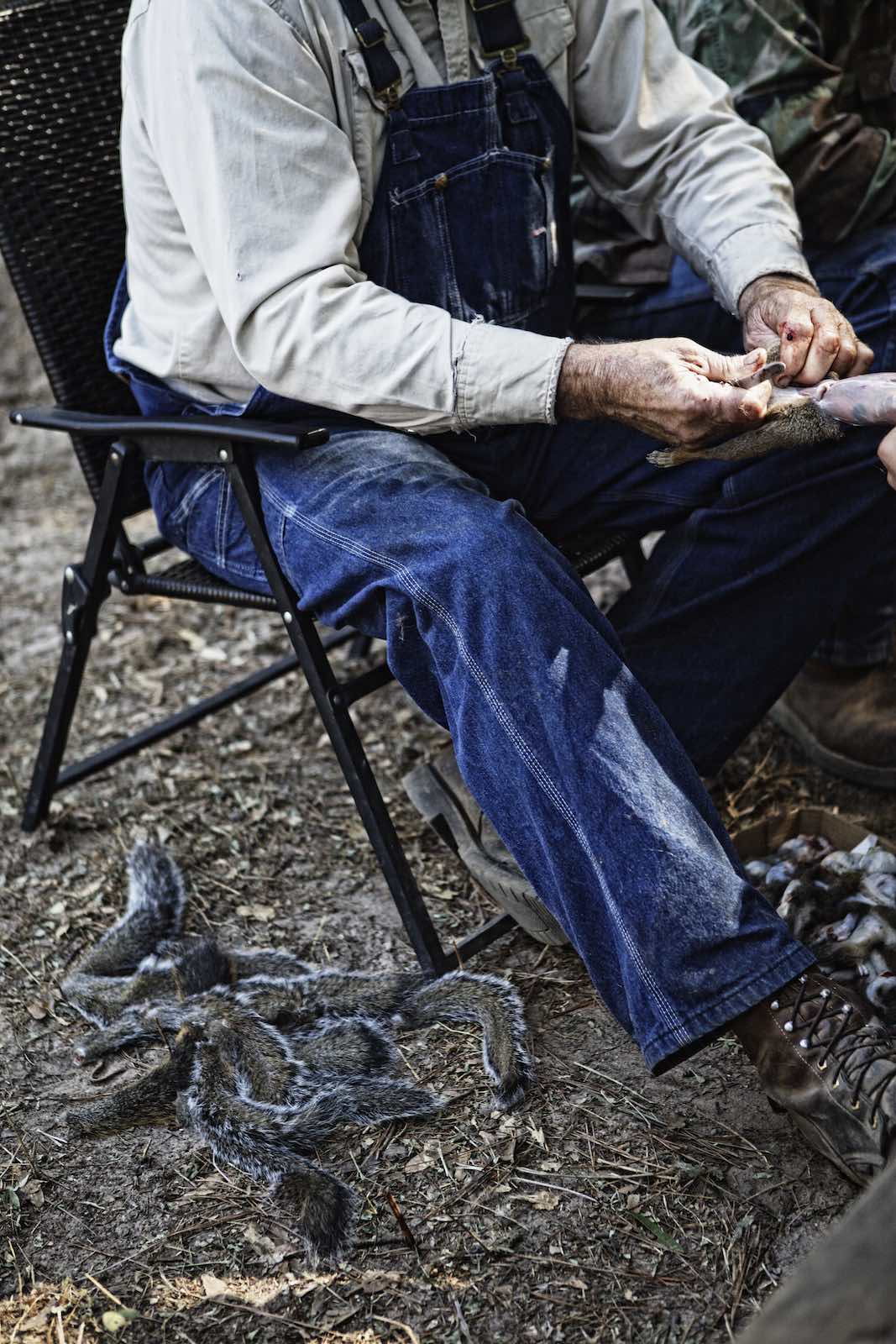 Jody Horton Photography - Hunter sitting next to squirrel tails while skinning the hunt. 